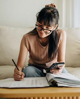 Woman using phone and writing down numbers.